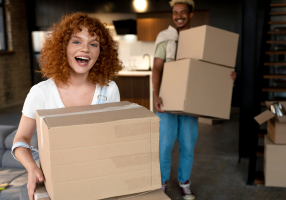 Porque comprar ou alugar com a nossa imobiliária? Flexibilidade para locações Casal feliz carregando caixas de mudança